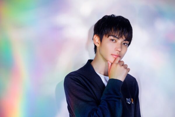 虹色のようなカラフルな背景の前で顎に手を添え柔らかく微笑む若い男性俳優のポートレート写真イメージ