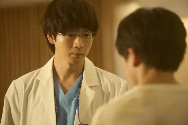 ドラマで白衣を着た男性医師が真剣な表情で相手と向き合っているシーン。医療ドラマで活躍する俳優のイメージ写真として、最新の出演情報や年収解説記事に使えるビジュアル。