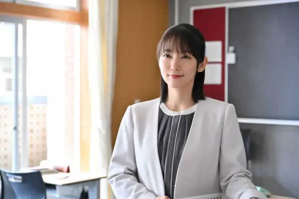 スーツ姿で教室に立ち穏やかに微笑む女性俳優のイメージ写真