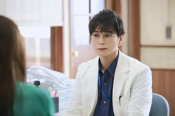 白衣を着た眼鏡の男性俳優が診察室で患者と向き合う場面の写真｜医師役ドラマで活躍する人気俳優の今年の出演情報と年収を解説するイメージ