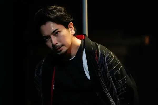 黒い和装風の衣装をまとった男性俳優が舞台上で鋭い表情を見せるアップ写真｜舞台や映画で評価が高まった時期の活躍をイメージしたビジュアル