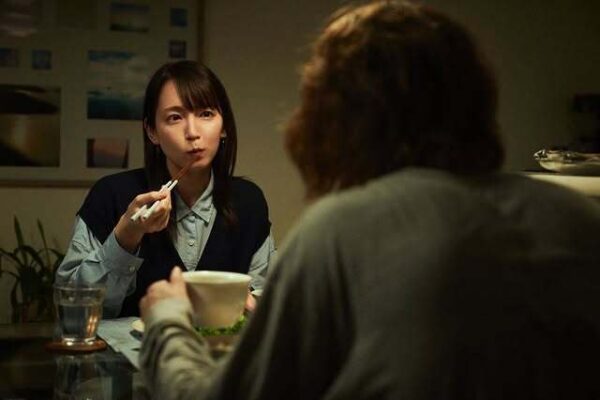 食卓で箸を持ちながら会話する女性俳優と男性の映画シーンの一コマ