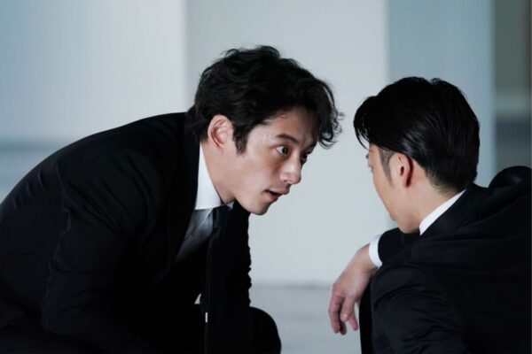 スーツ姿で相手と向き合い緊張感ある表情を見せる坂口健太郎のドラマスチール