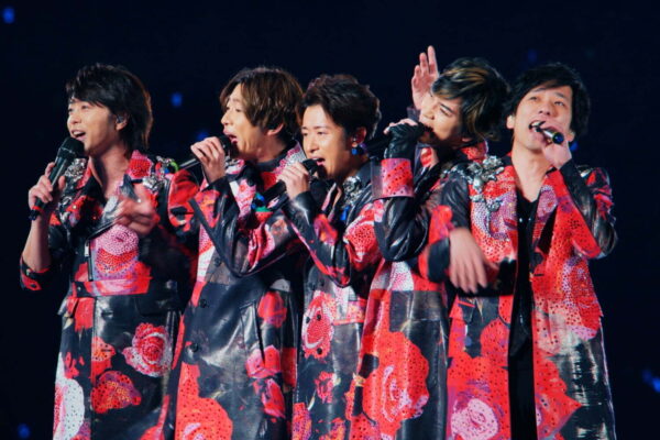 赤い衣装を着た男性アイドルグループがステージで歌うライブシーン｜国民的グループとしての人気とメンバー個人の年収推移を紹介するための写真