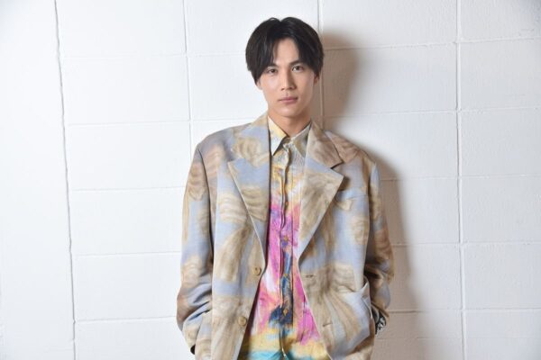 白い壁の前でカラフルなスーツを着た男性俳優のポートレート（プロフィール用宣材）