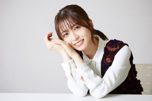 インタビューで机に腕を乗せて笑顔を見せる若い女性タレントの宣材風ポートレート写真