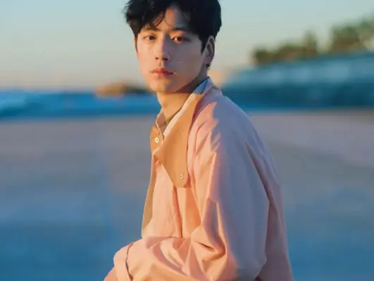 海辺で夕景を背景にたたずむ坂口健太郎のポートレート