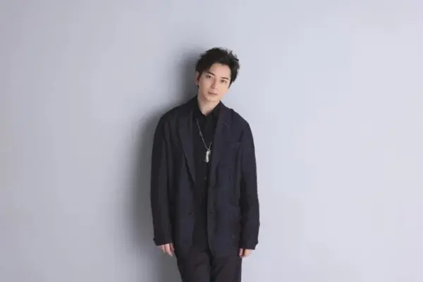 シンプルなグレー背景の前に黒いジャケット姿で立つ若手俳優の全身写真｜落ち着いた雰囲気の男性俳優のプロフィールと経歴を紹介するためのイメージカット