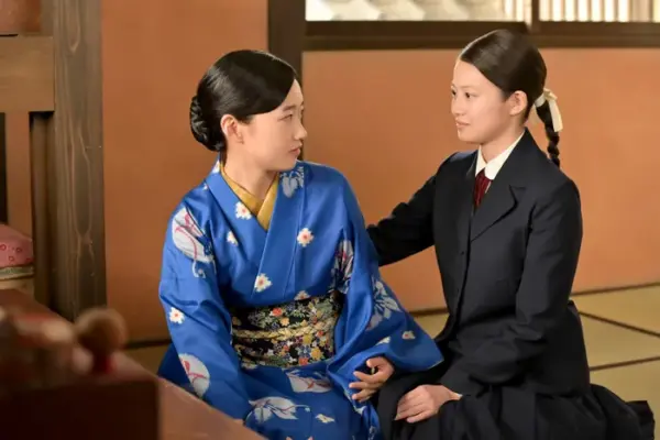 畳の和室で青い着物の女性と黒い制服姿の女性が向き合い、肩に手を添えて会話する場面