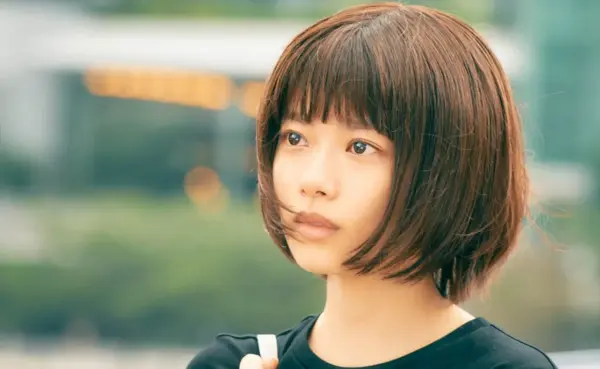 屋外で遠くを見つめるボブヘアの若い女性のクローズアップ、柔らかな玉ボケ背景のポートレート