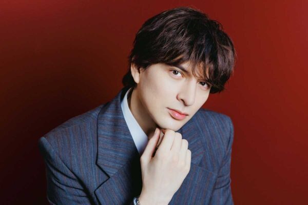 赤い背景でスーツ姿の城田優のポートレート写真｜俳優・歌手としての経歴と年収を解説するプロフィール画像