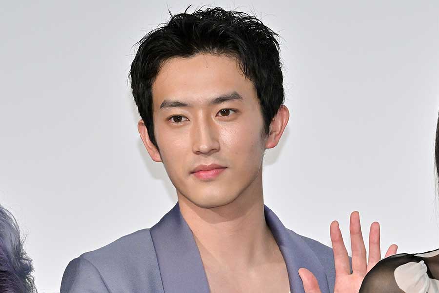 イベント会場でジャケット姿の男性が手を上げて挨拶する記者会見風の写真（アイキャッチ画像）