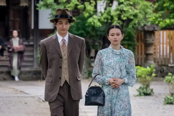 スーツ姿の男性と花柄ワンピースの女性が並んで歩くドラマシーン・レトロな雰囲気の街並みを背景にした今年の出演作品イメージカット
