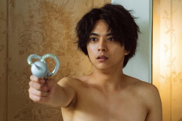 淡いライティングの中でブルーのシャツを着た男性が腕を上げてこちらを見つめるアップ写真。雑誌インタビュー風の雰囲気を伝える画像