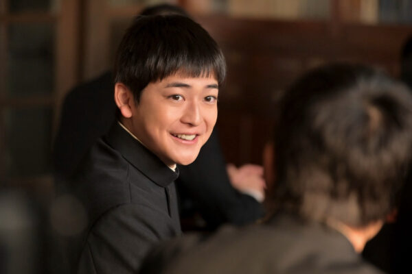 高橋文哉がドラマの撮影中に微笑んでいるシーン。2024年の年収推定に関連する活動の一環としての出演シーン。