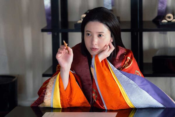 華やかな和装で机に向かい考え込む女性俳優のドラマシーン写真（出演作イメージの挿絵）