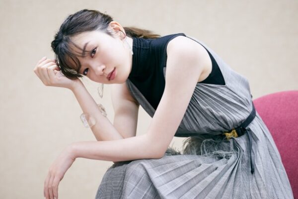 グレーのワンピースで椅子に座る女性のポートレート。横顔気味の落ち着いた表情でインタビューカット風。