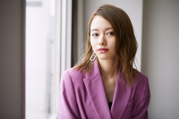 大きな窓際でカメラを見つめるパープルのジャケットを着た若い女優のポートレート・落ち着いた表情でキャリアや経歴紹介ページに適した画像