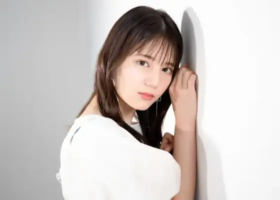 白いブラウス姿の女性モデルが壁にもたれ、真正面から少し憂いを帯びた表情で見つめるアップのポートレート写真