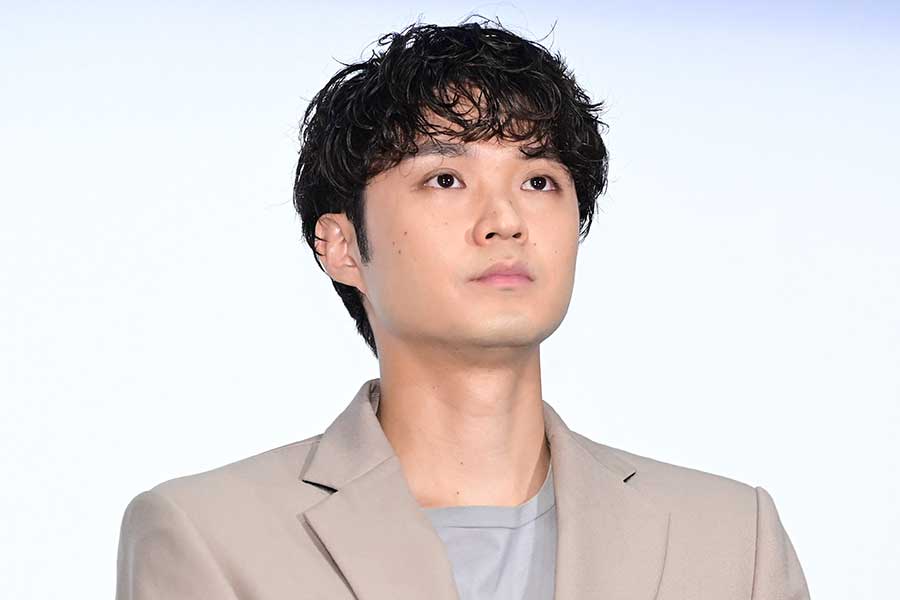 ベージュのジャケットを着た磯村勇斗がやや上を見上げるように正面を見ているバストアップ写真。柔らかい光で撮影されたアイキャッチ用の画像。