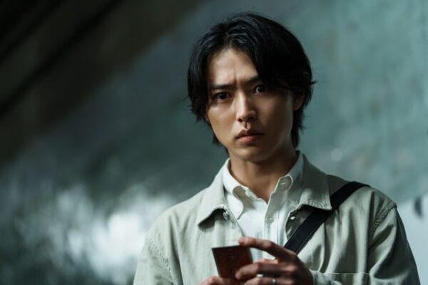 カードを手に真剣な表情の男性俳優。薄暗い通路での映画スチールカット