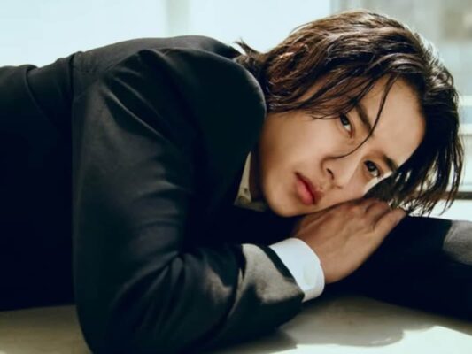 黒いスーツで横たわりカメラを見つめる男性のポートレート。柔らかな自然光のスタジオ撮影