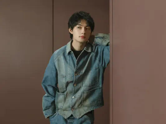 デニムジャケット姿で壁にもたれる佐野勇斗のポートレート写真（経歴紹介用）