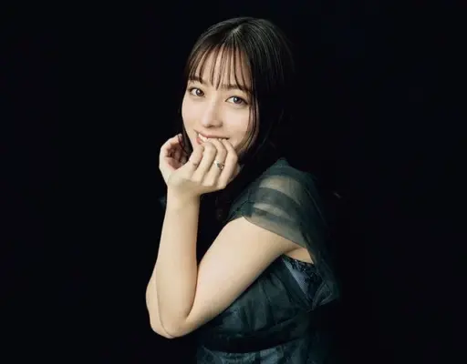 黒背景で微笑む若い女性のポートレート。指先に手を添えるポーズのアップ写真