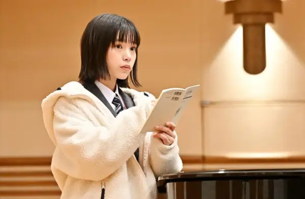 音楽ホールで楽譜を読む制服姿の當真あみのドラマシーン・音楽をテーマにした作品カット