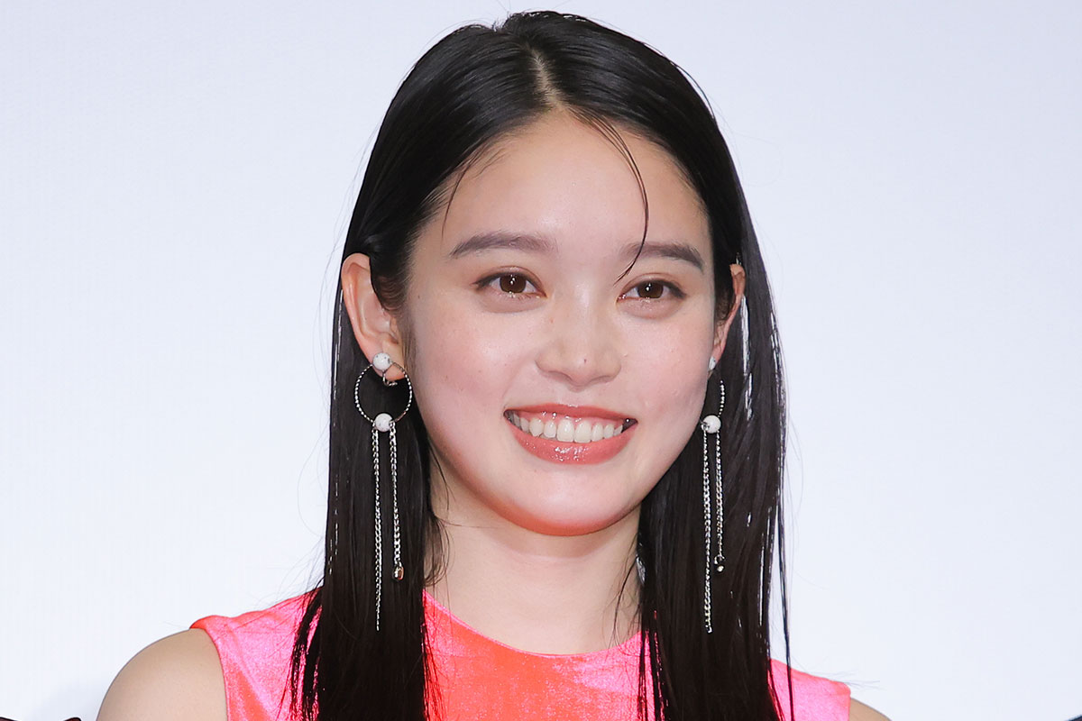 ピンクの衣装を着た女性のバストアップ写真。長いイヤリングを付け、明るい表情でカメラに向かって笑っている