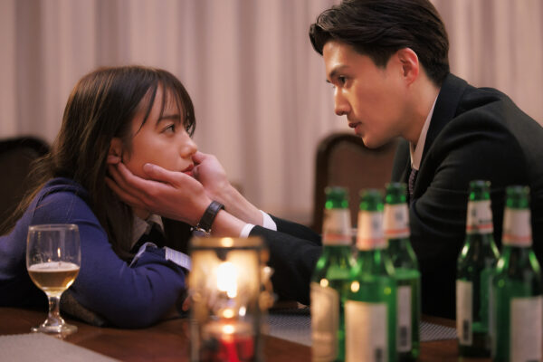 バーのテーブルでビール瓶に囲まれながら、スーツ姿の男性が女性の頬を両手で包み見つめ合う恋愛ドラマの緊迫したシーン