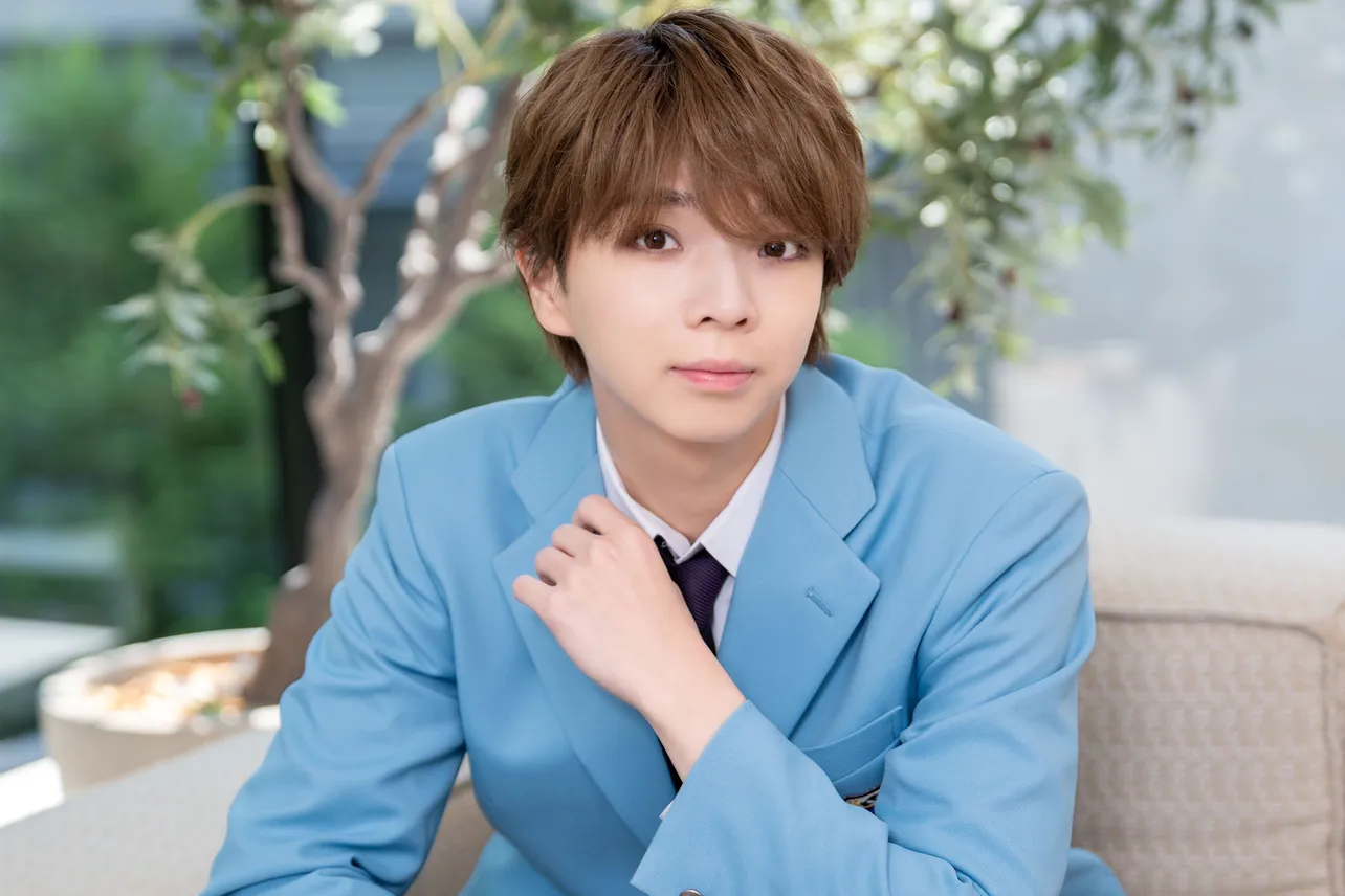 水色スーツ姿の若い男性がソファに座りカメラ目線で微笑む屋外風ポートレート（アイキャッチ画像）